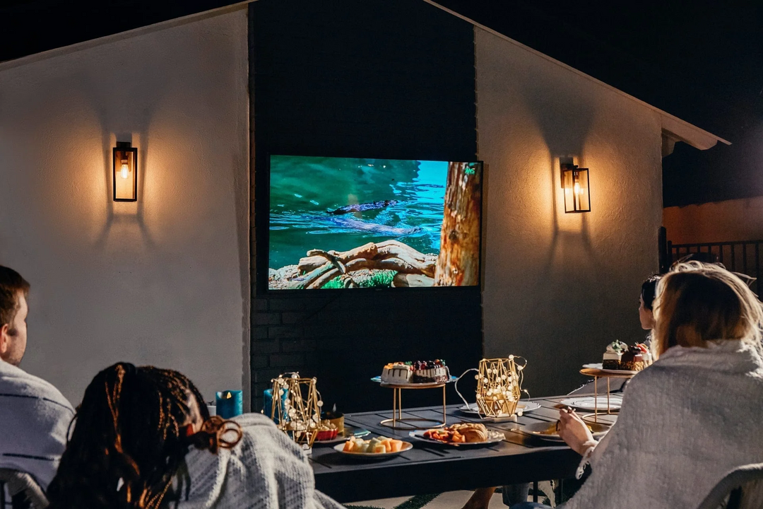 Family watching NFL game on Sylvox outdoor TV on balcony during cold weather