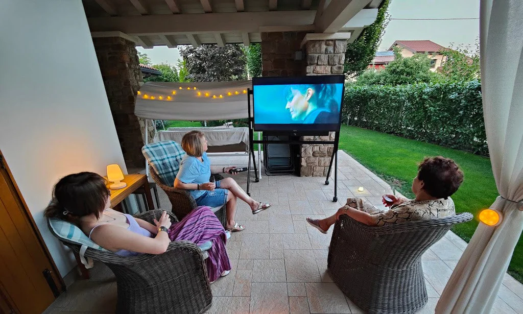 Multi-generational family laughing during backyard movie night, immersed in a bright 55-inch Sylvox outdoor TV's cinematic display